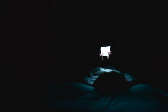 Face illuminated by blue light of phone in dark
